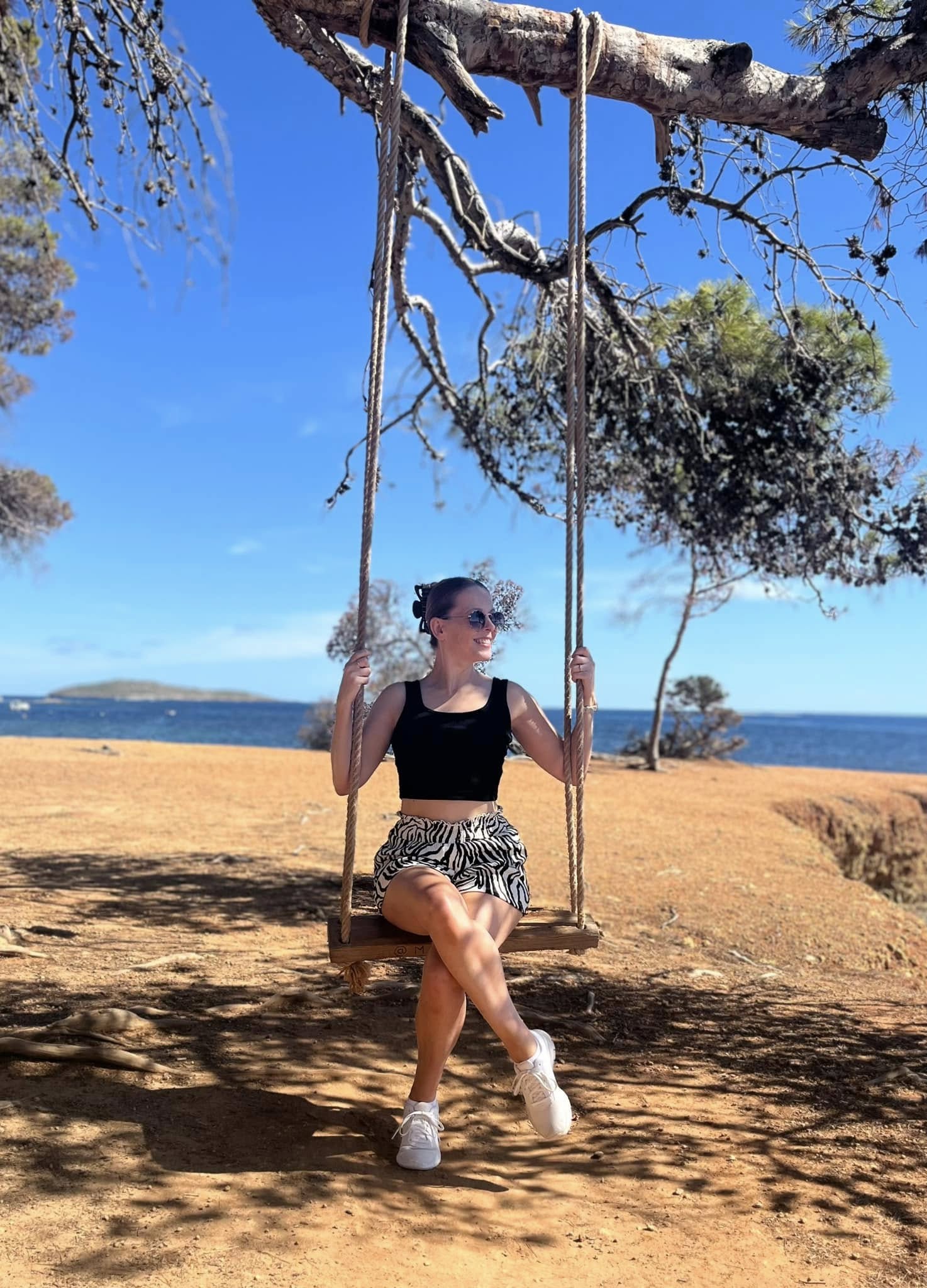 girl sitting on a swing hung from a branch with the sea behind her