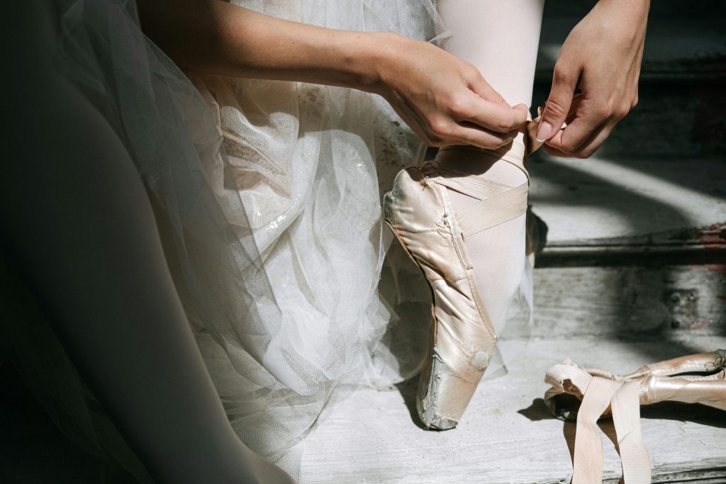 Ballerina preparing for performance, tying pointe shoes in soft natural light.